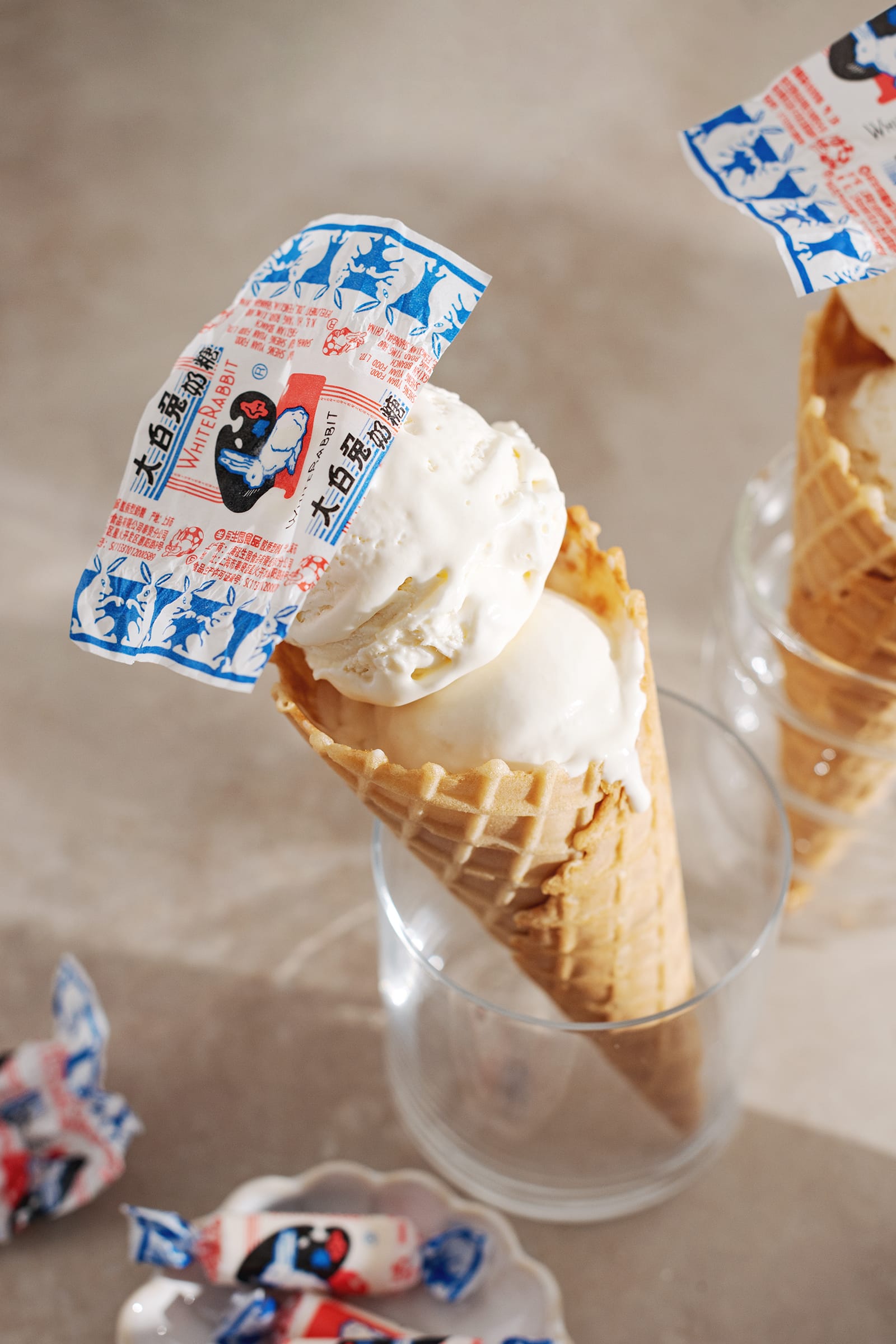 White rabbit ice cream cone in a glass with candy wrapper on top of it.