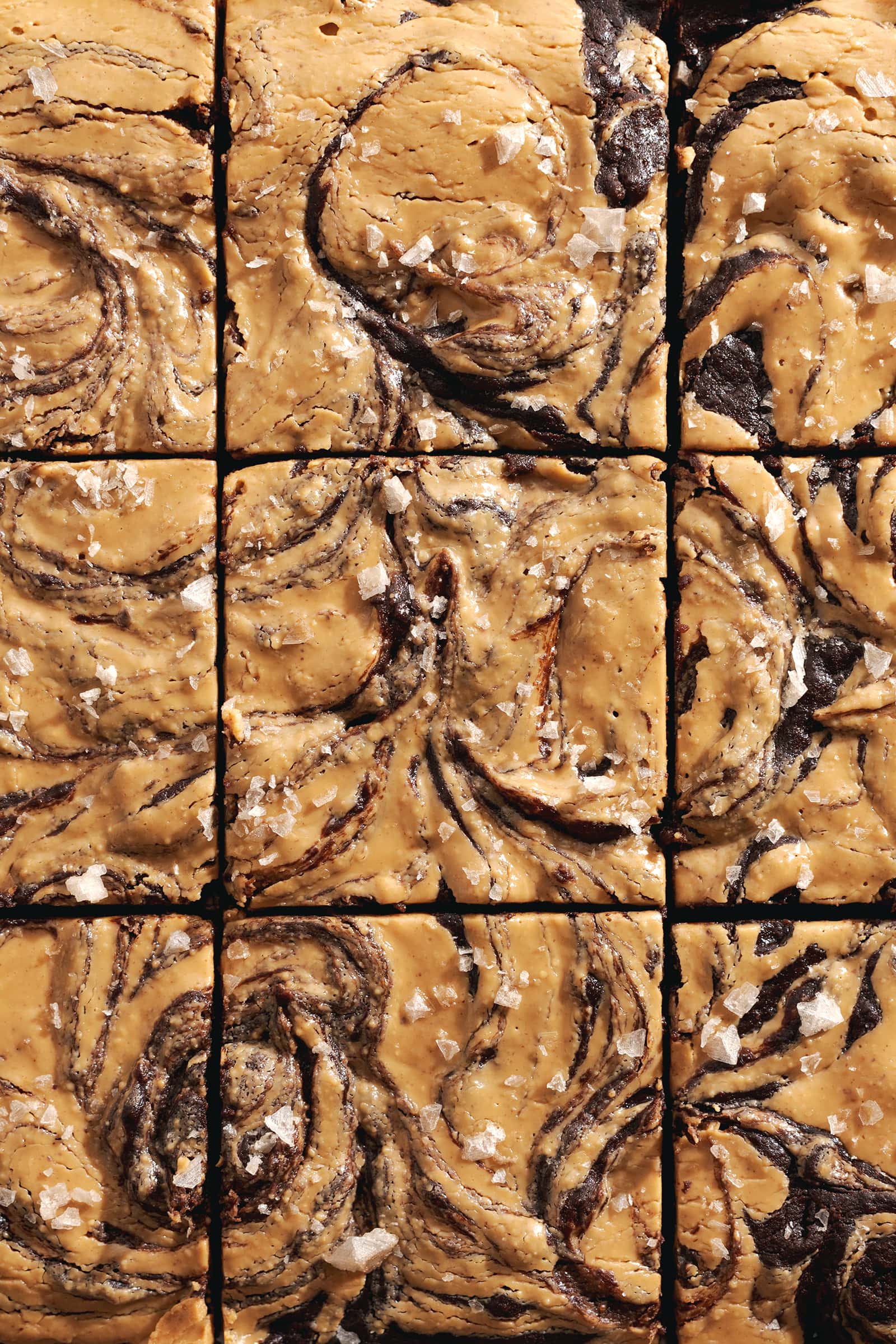 Top down view of brownie squares with peanut butter swirls and flaky salt on top.