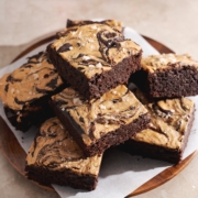 A stack of peanut butter brownies on a plate with mugs in the back.