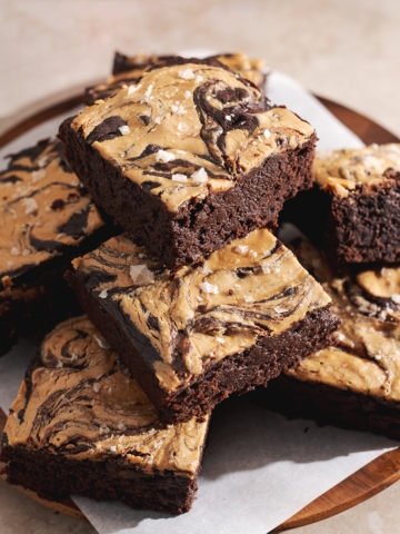 A stack of peanut butter brownies on a plate with mugs in the back.