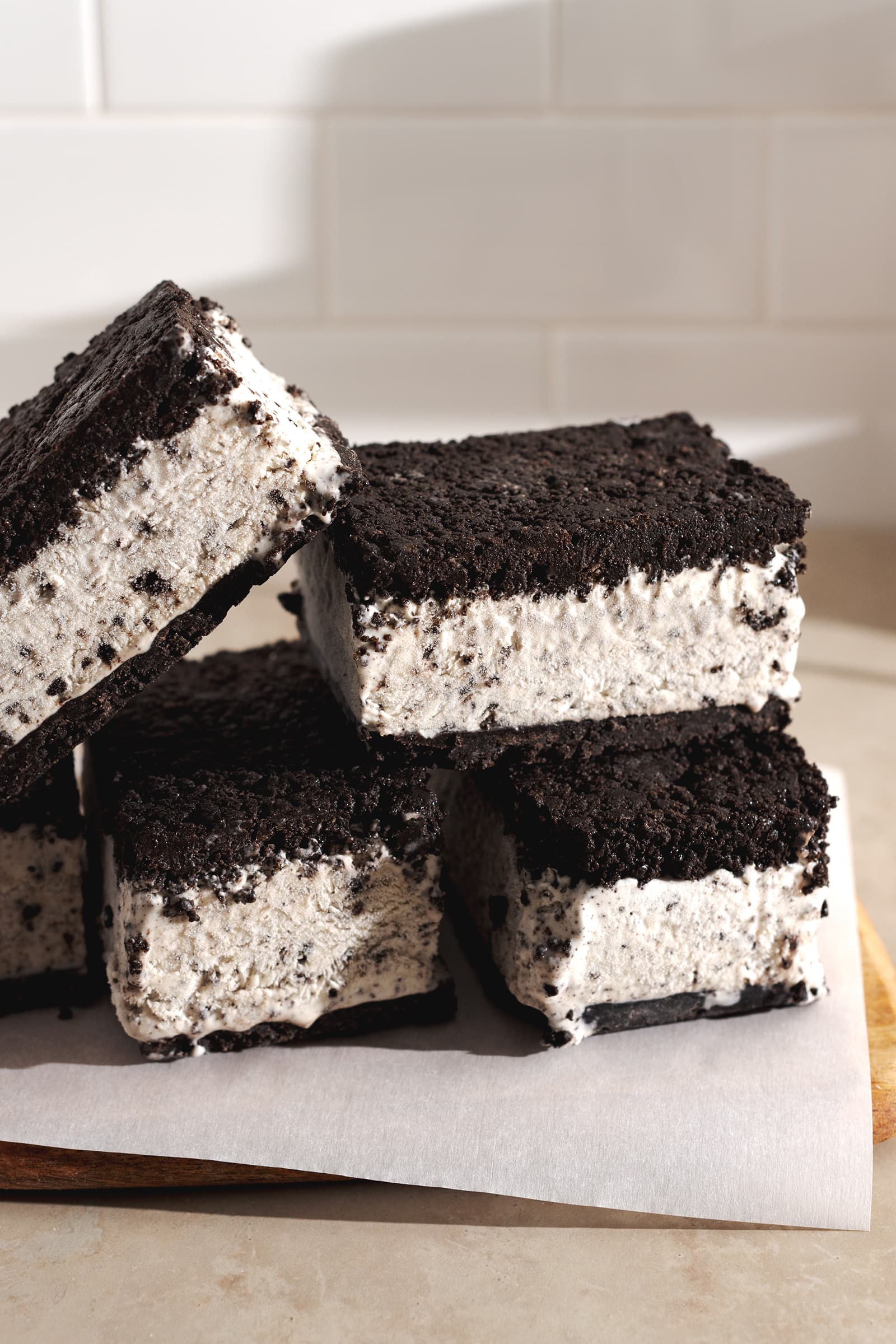 Oreo ice cream sandwiches stacked on top of each other on parchment paper.