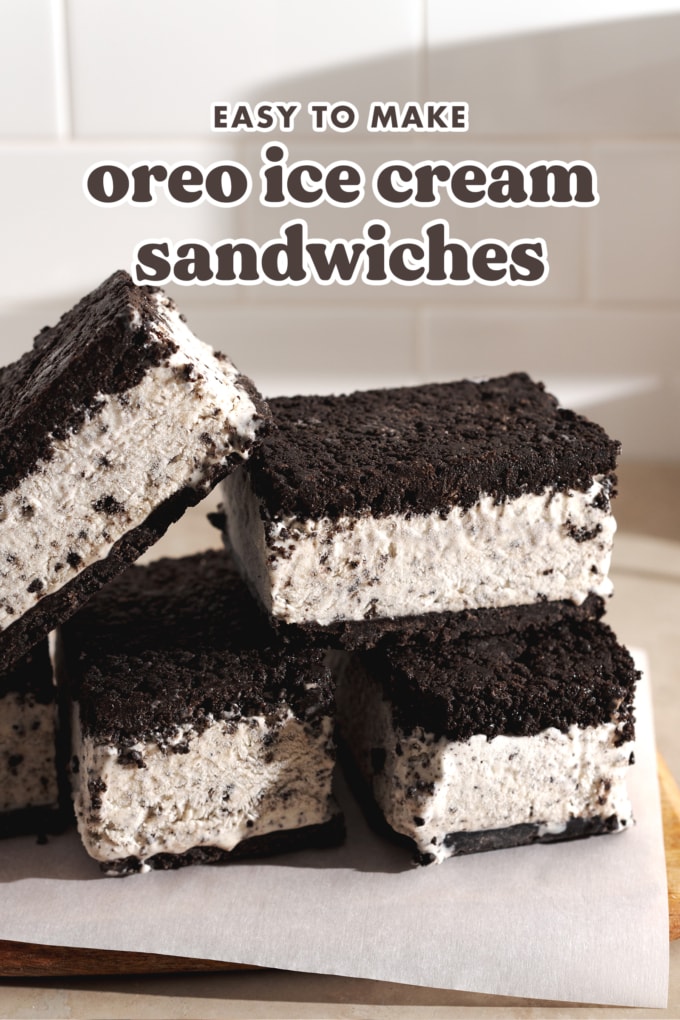 Oreo ice cream sandwiches stacked on top of each other on parchment paper.