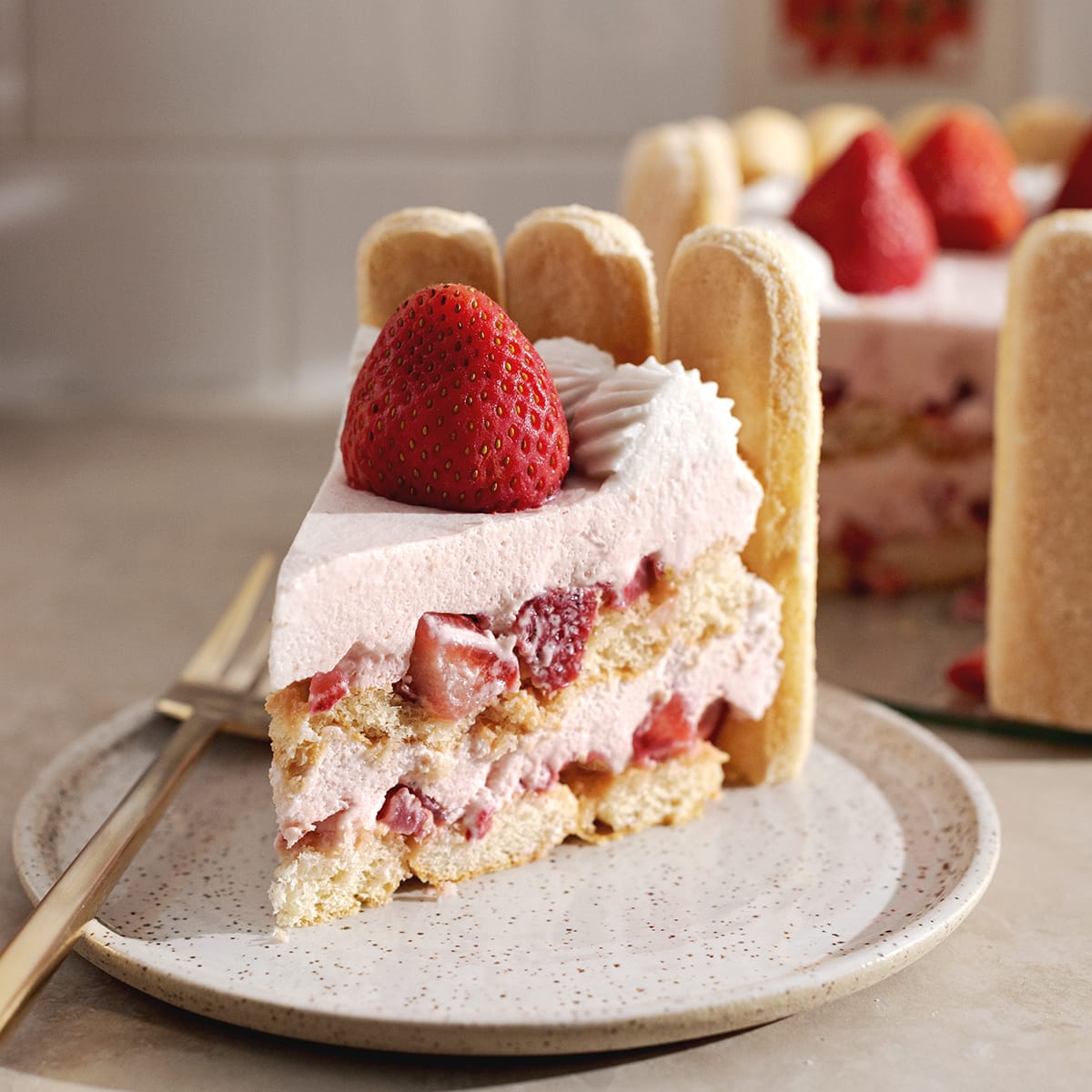 A slice of strawberry charlotte cake on a plate showing the layers and whole strawberry on top.