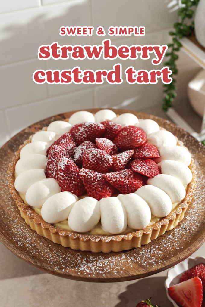 Strawberry custard tart topped with dollops of whipped cream and layers of strawberries on a wooden plate.