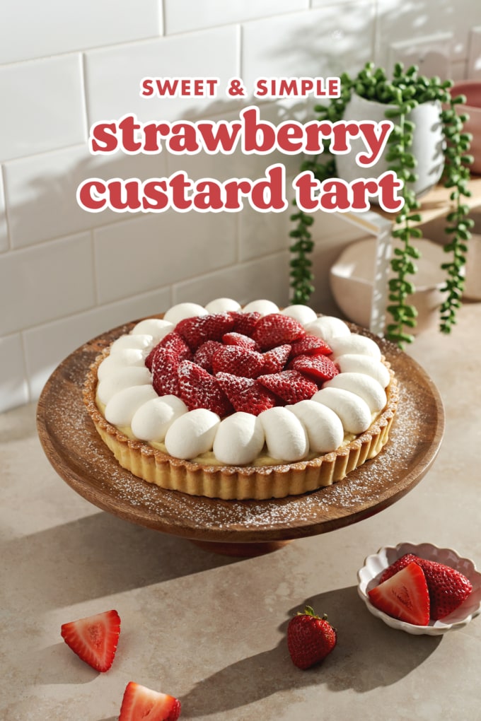 Strawberry tart on a wooden cake stand with strawberries scattered on tabletop.