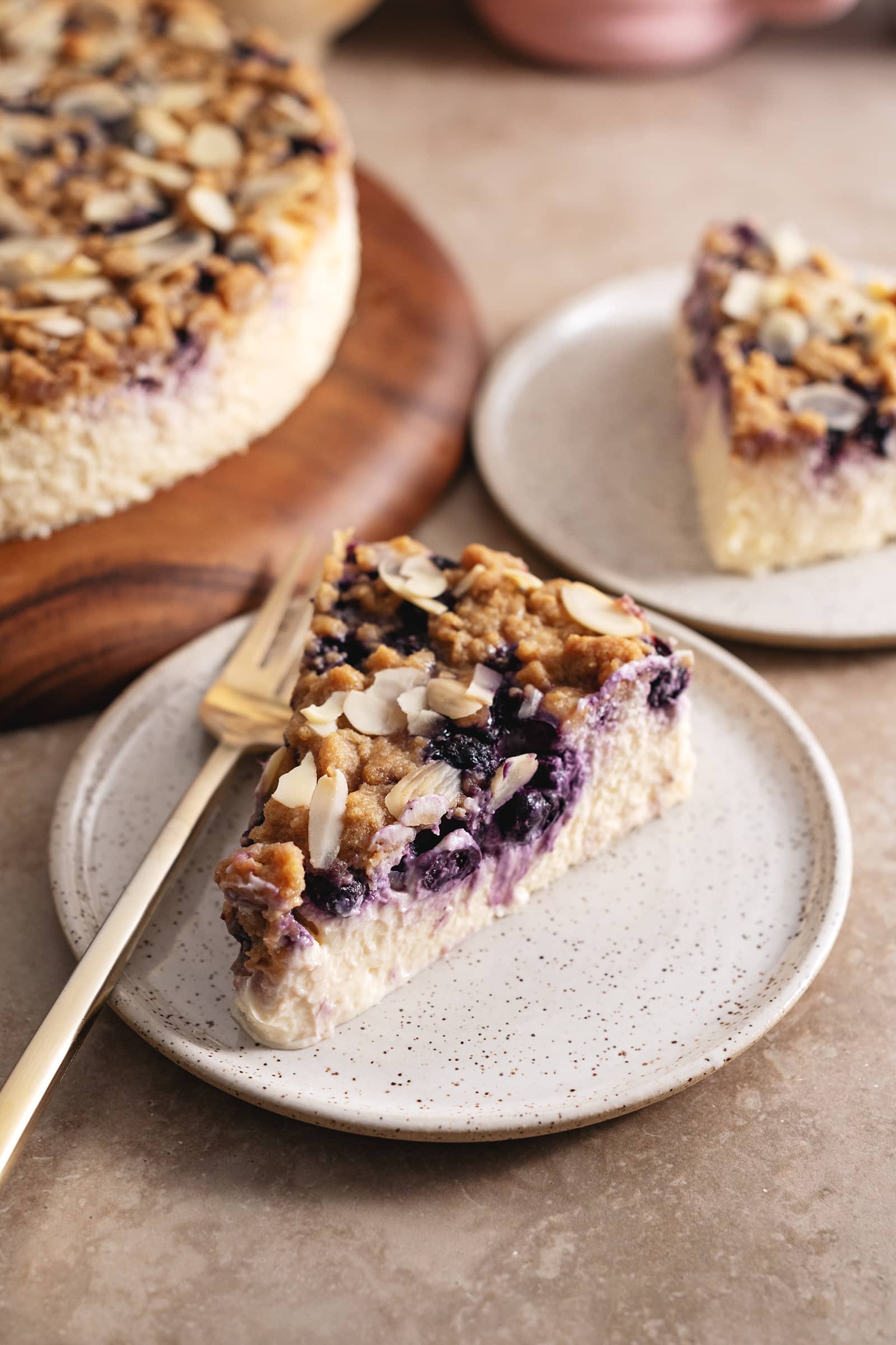 A slice of blueberry crumble cheesecake on a plate with a fork showing the layer of blueberries inside.