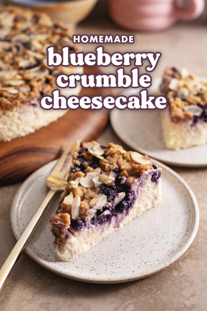 A slice of blueberry crumble cheesecake on a plate with a fork showing the layer of blueberries inside.