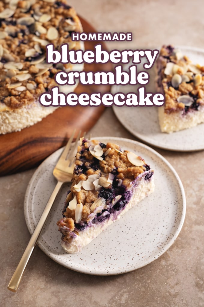 A slice of blueberry crumble cheesecake on a plate with a fork with the cheesecake in the background.