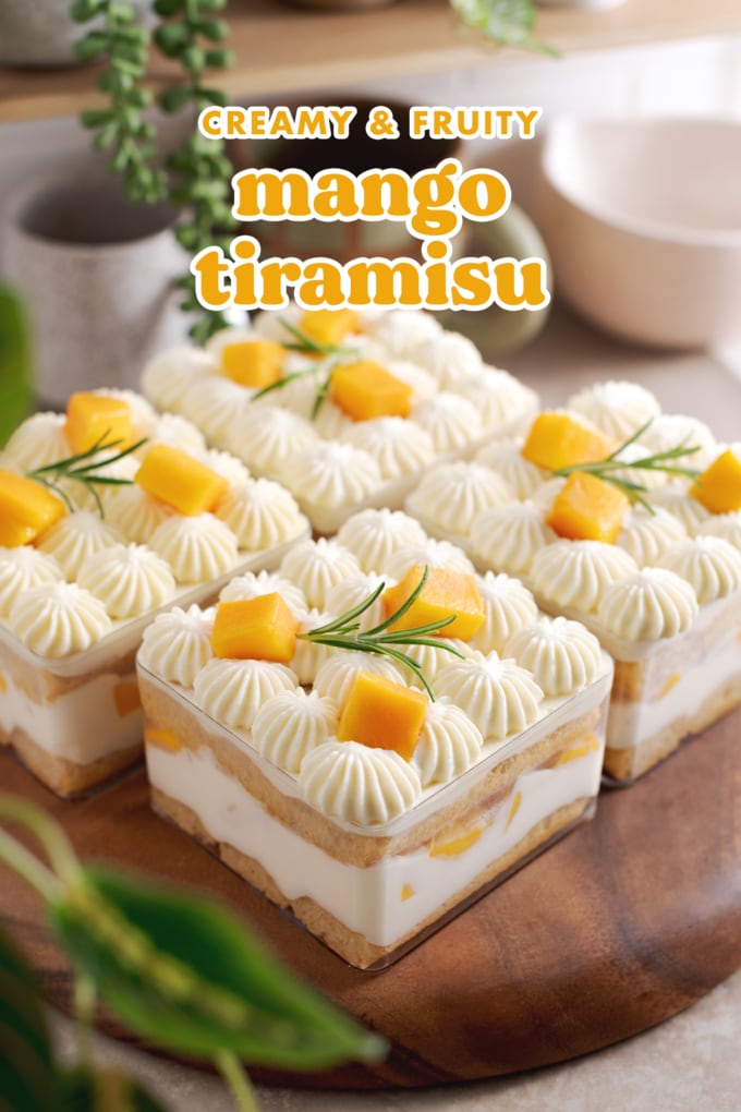 Four containers of mango tiramisu on a wooden platter with greenery around it.