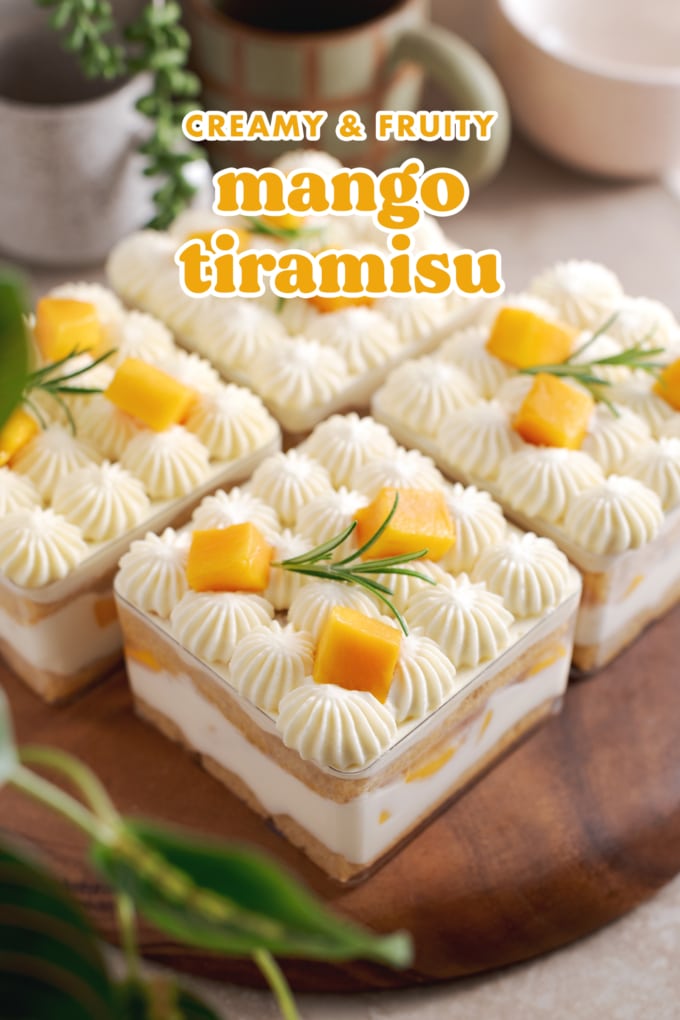 Four containers of mango tiramisu on a wooden platter with greenery around it.