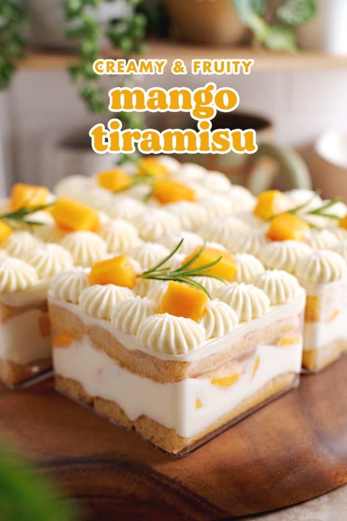Square container of tiramisu with the layers of ladyfingers, mascarpone cream, and mangoes showing through the sides.