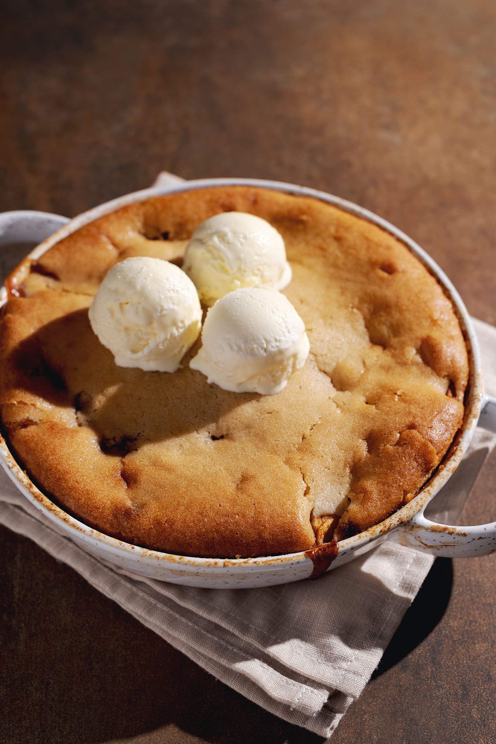 Baking dish of peach cobbler with three scoops of ice cream on top.