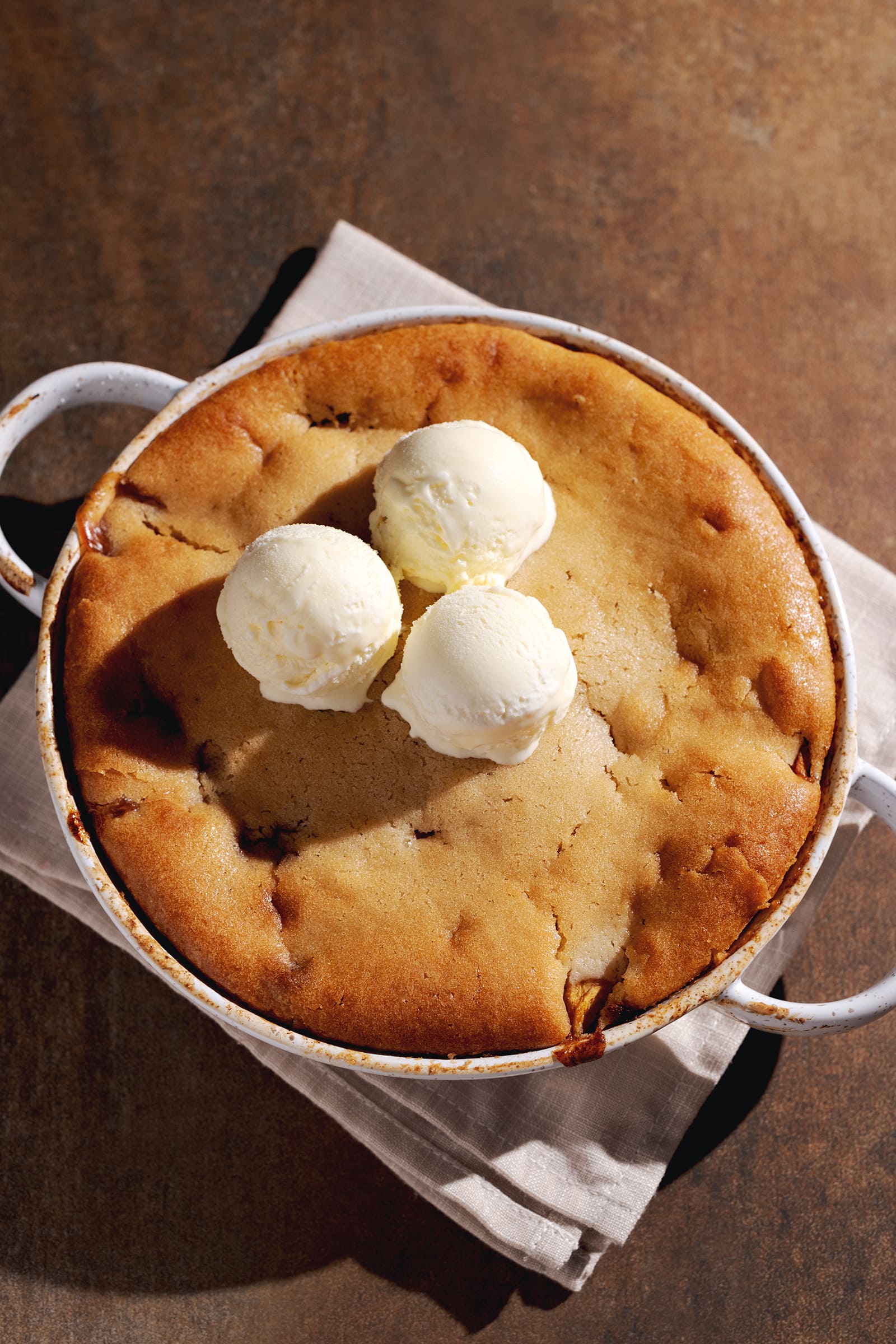 Top down view of a peach cobbler in a round baking dish with three scoops of ice cream on top.