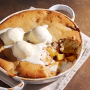 A dish of peach cobbler with a scoop taken out of it to show the peach filling inside.