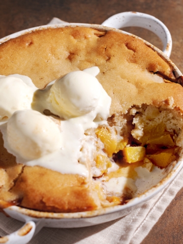 A dish of peach cobbler with a scoop taken out of it to show the peach filling inside.