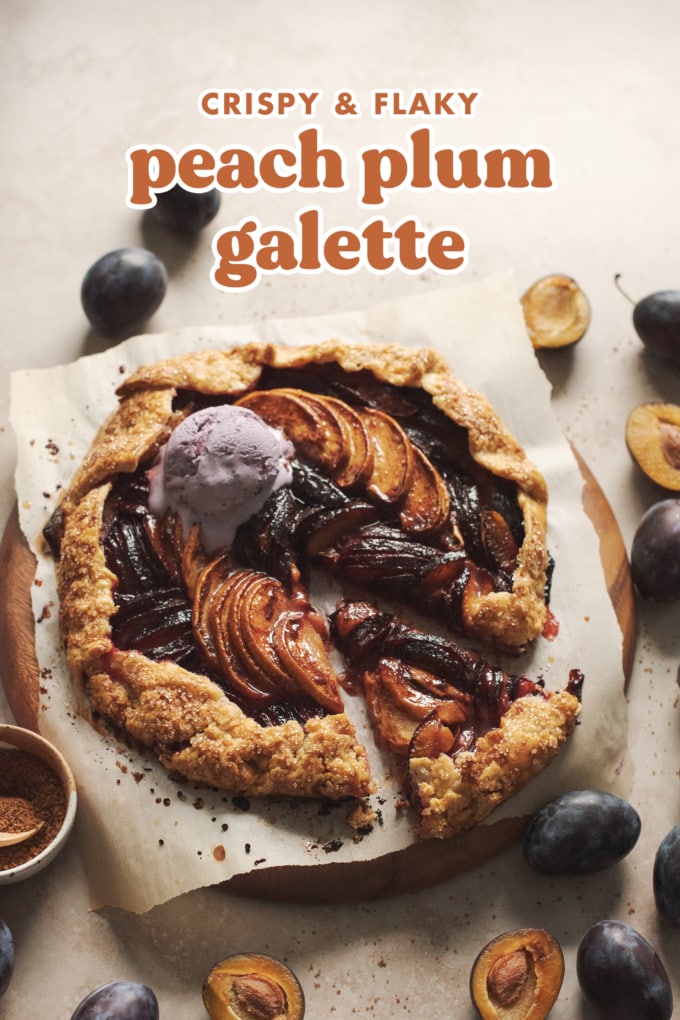 Peach plum galette on a wooden platter with plum scattered around it.