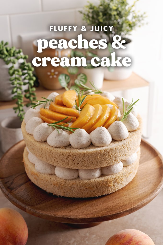 Two-layer peaches and cream cake on a wooden cake stand surrounded by peaches and plants.