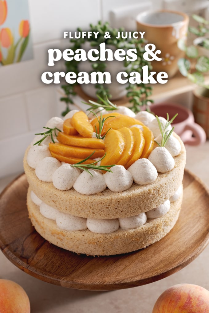 Two-layer peaches and cream cake on a wooden cake stand on kitchen counter.