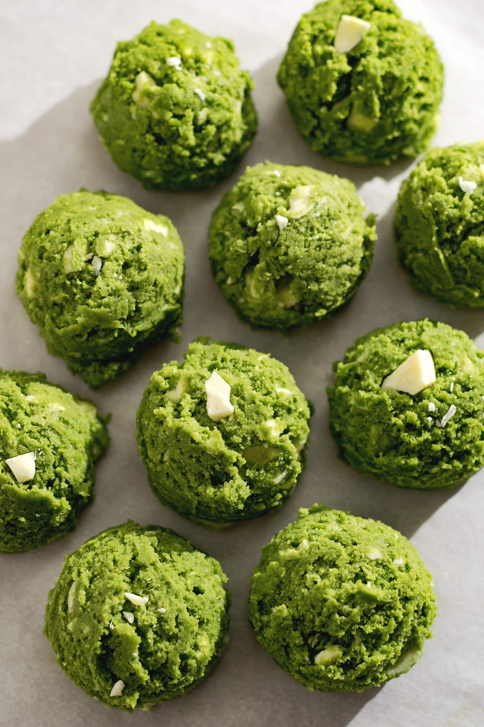 Balls of matcha cookie dough on parchment paper.
