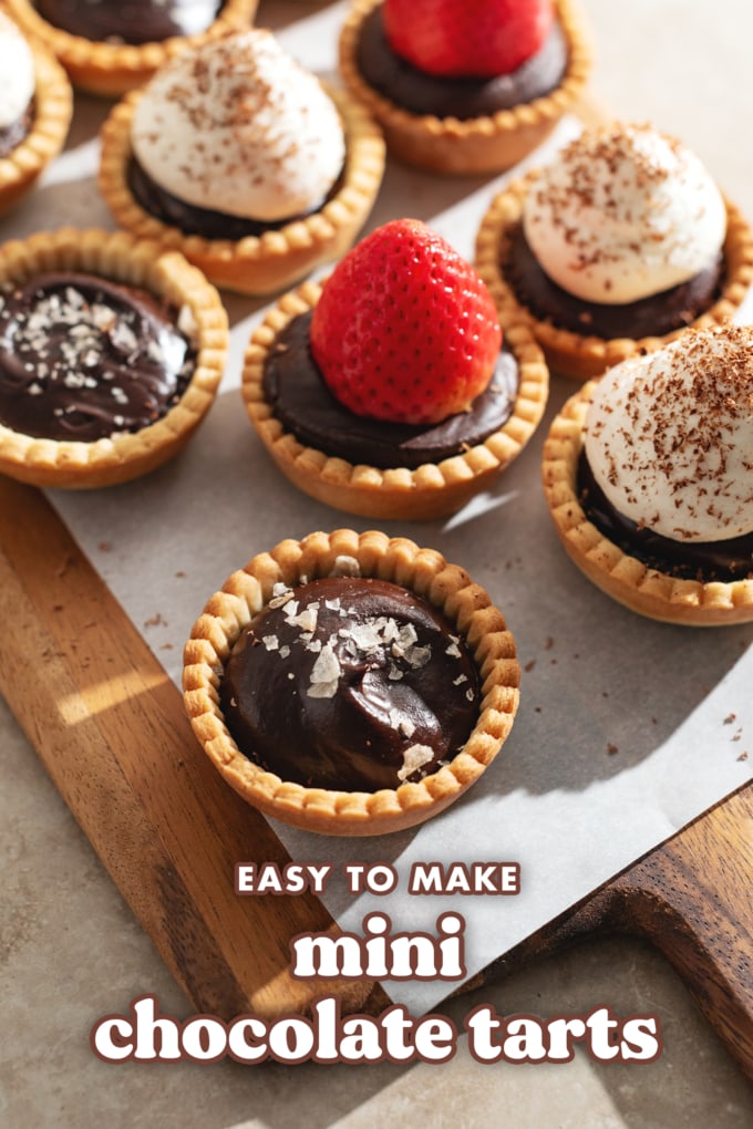 A mini chocolate tart topped with flaky salt in front of other tarts.