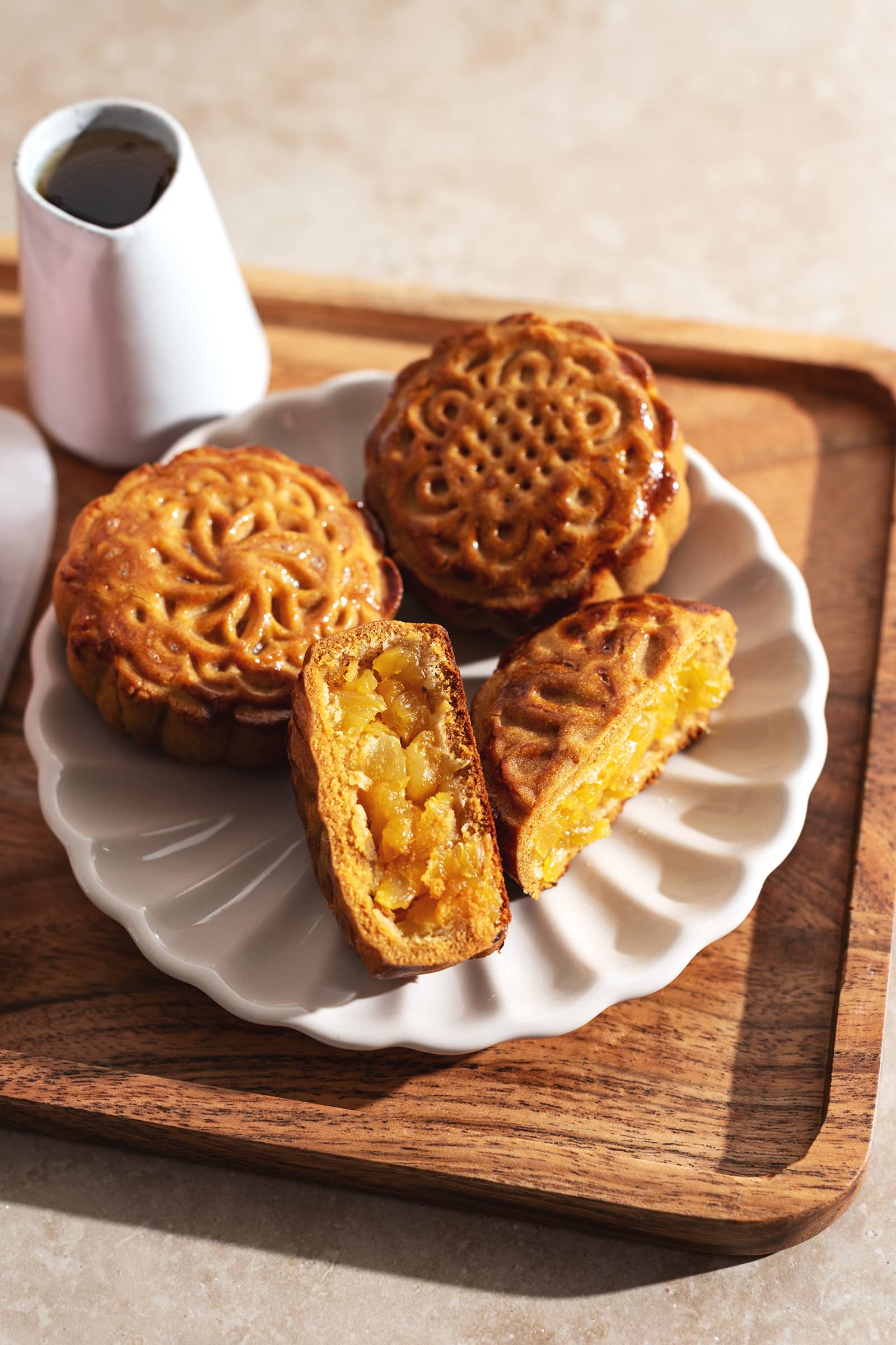 A pineapple mooncake cut in half on a plate with two other mooncakes.