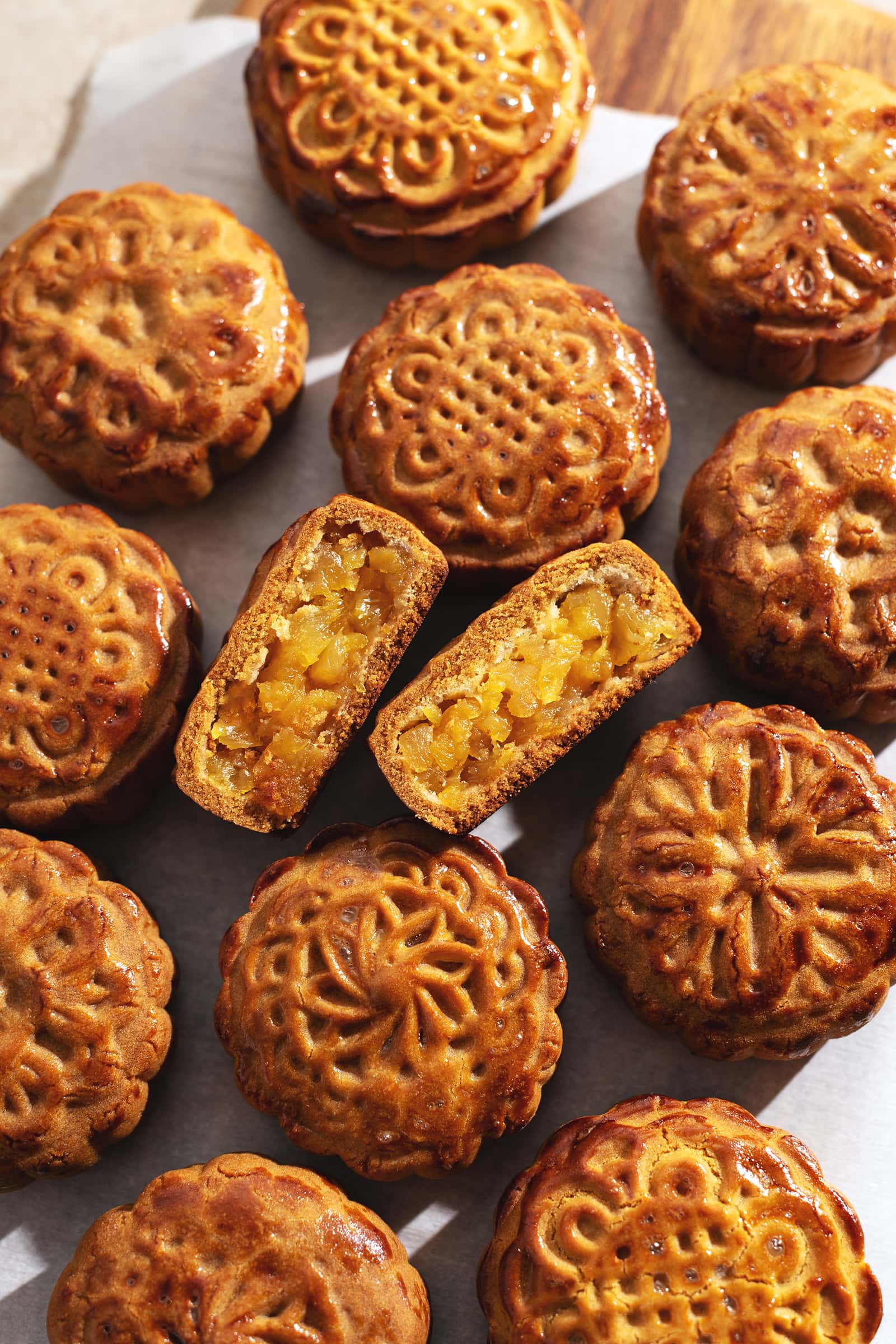 A pineapple mooncake cut in half to show filling inside in the middle of several other mooncakes.