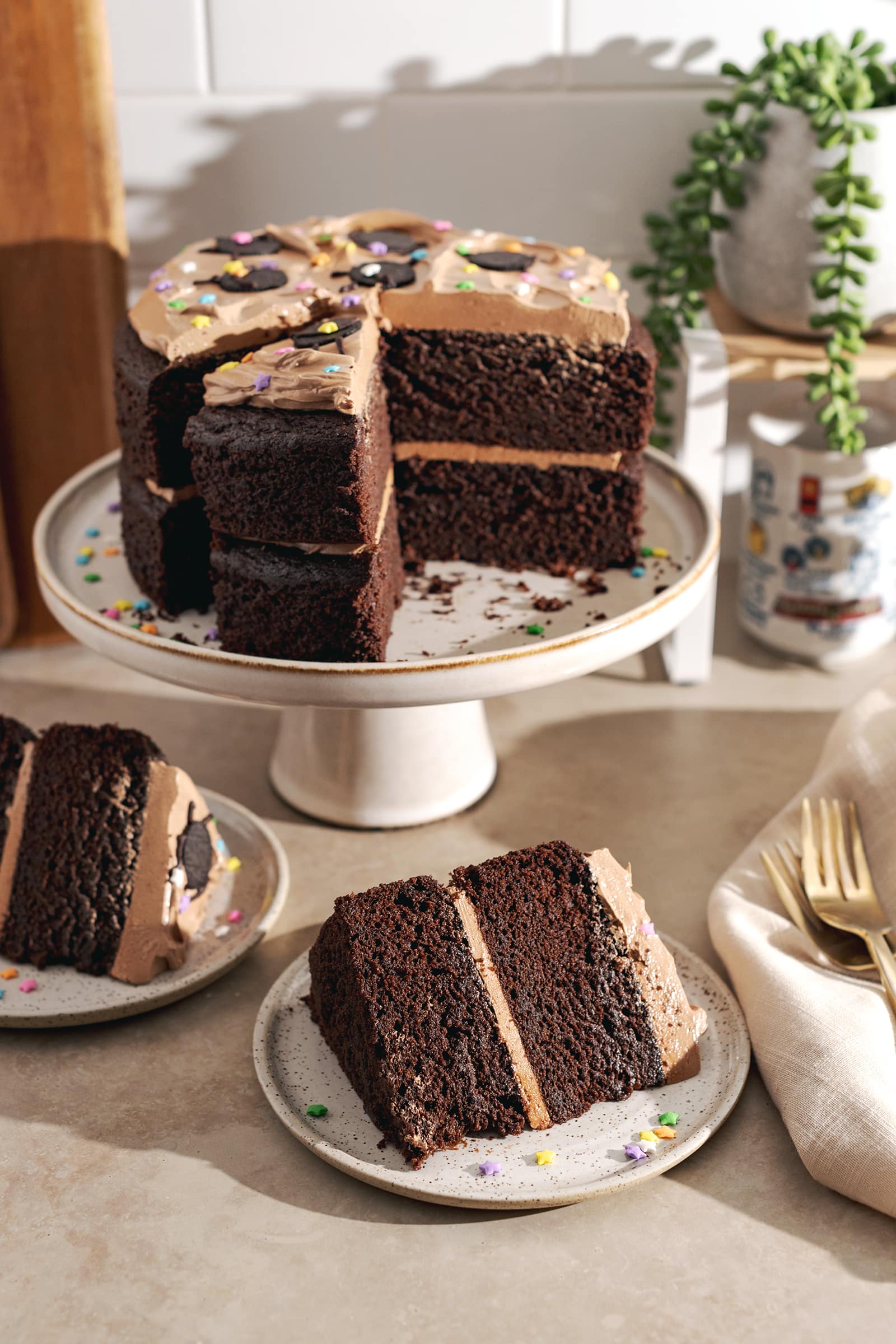 Slices of chocolate cake on plates in front of the soot sprite cake on a cake stand.