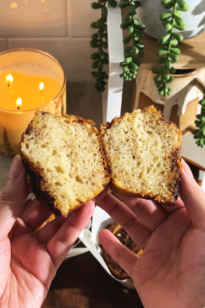 Hands holding a muffin cut in half to show the texture inside.
