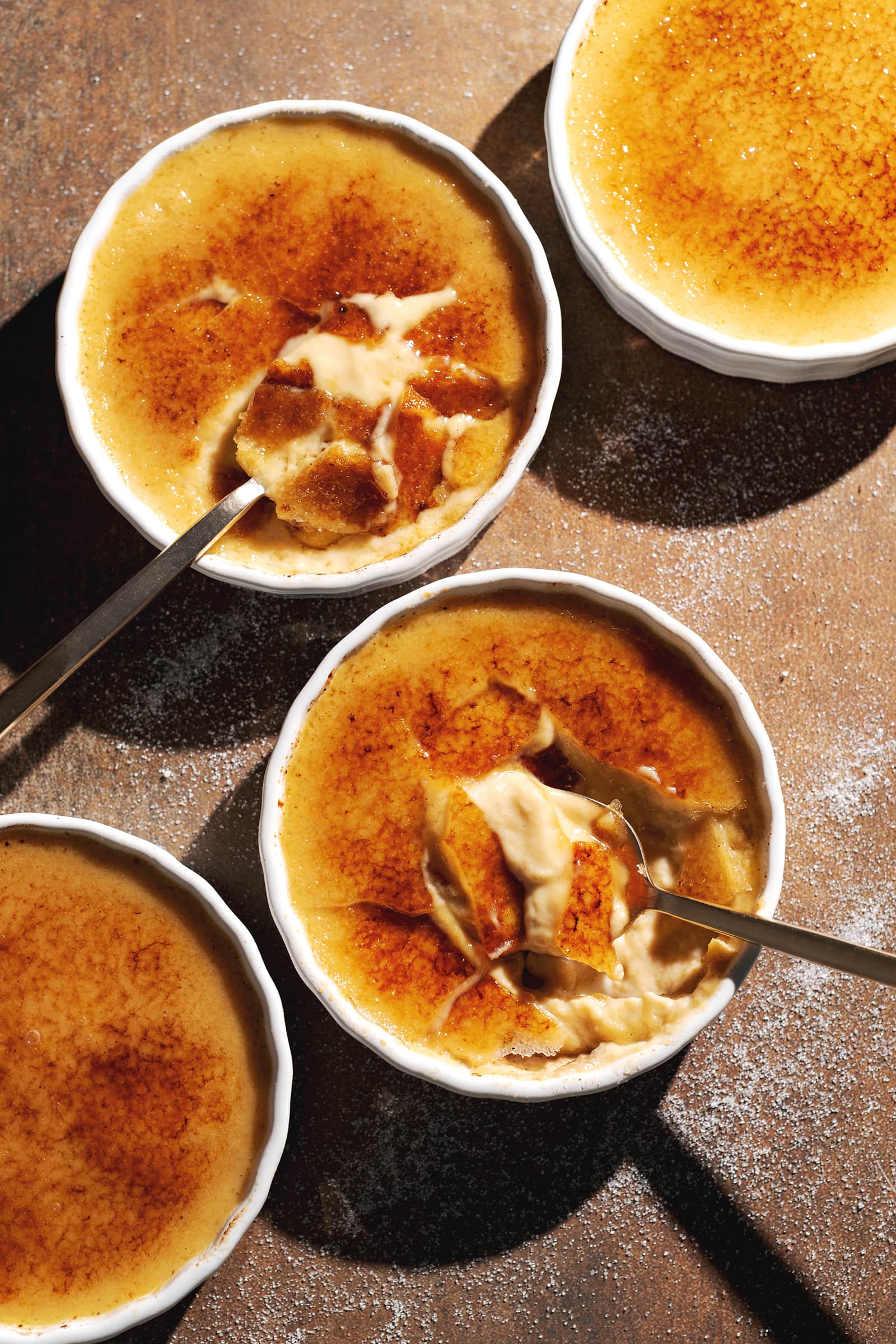 Four ramekins of pumpkin crème brûlée with torched sugar toppings.
