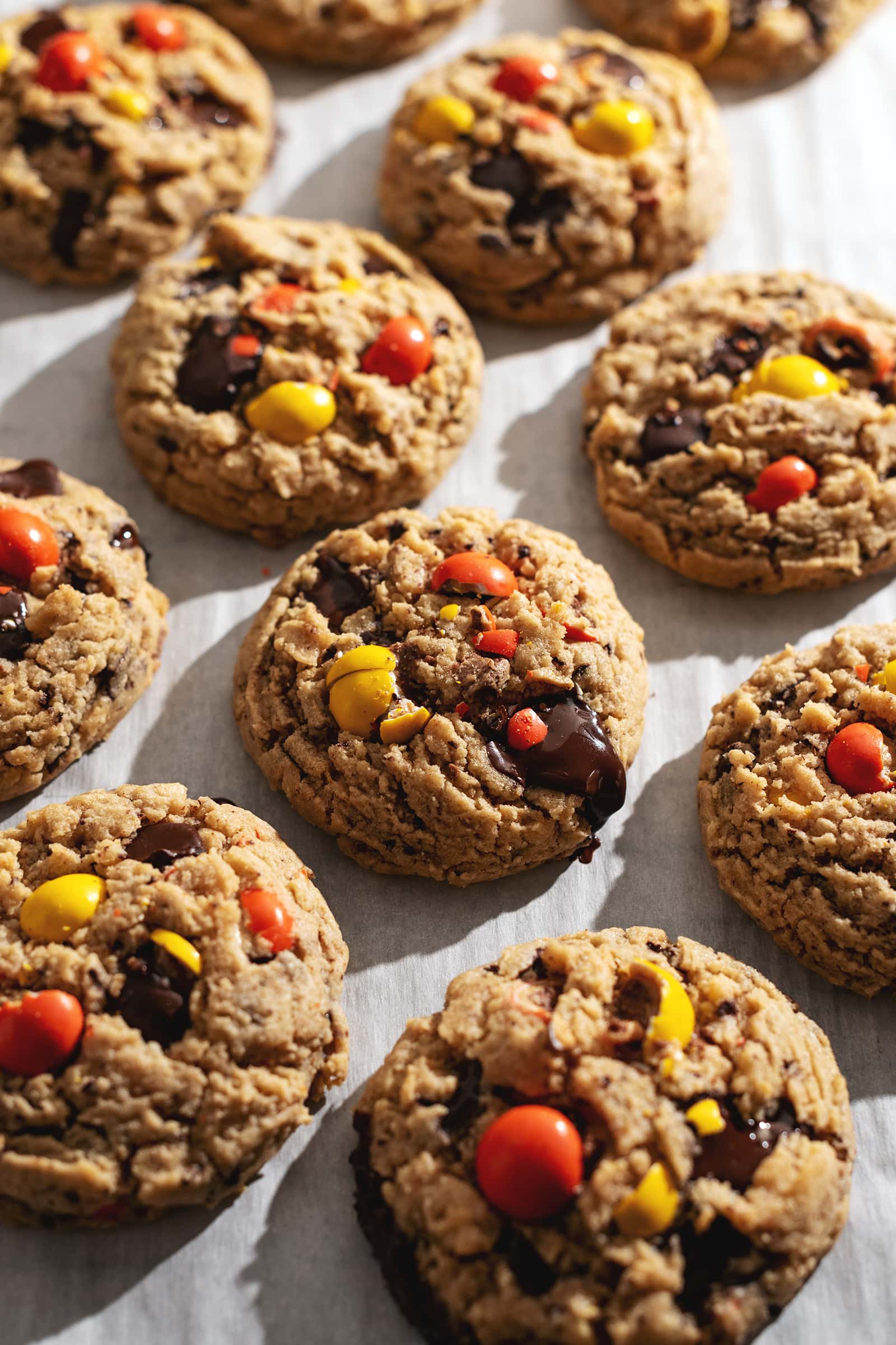 Cookies topped with chocolate and reese's pieces candy on parchment paper.