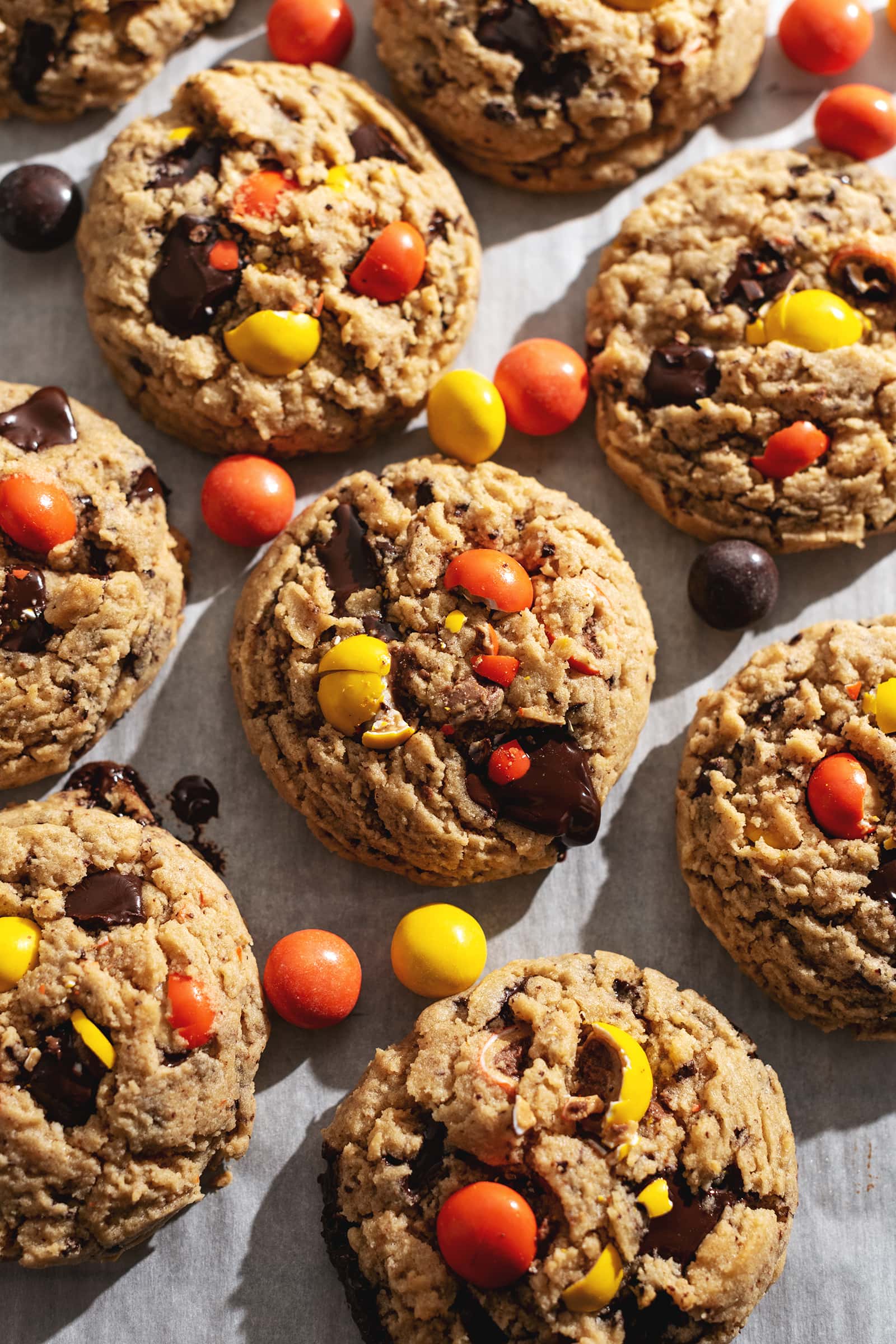 Cookies and reese's pieces candy scattered on parchment paper.