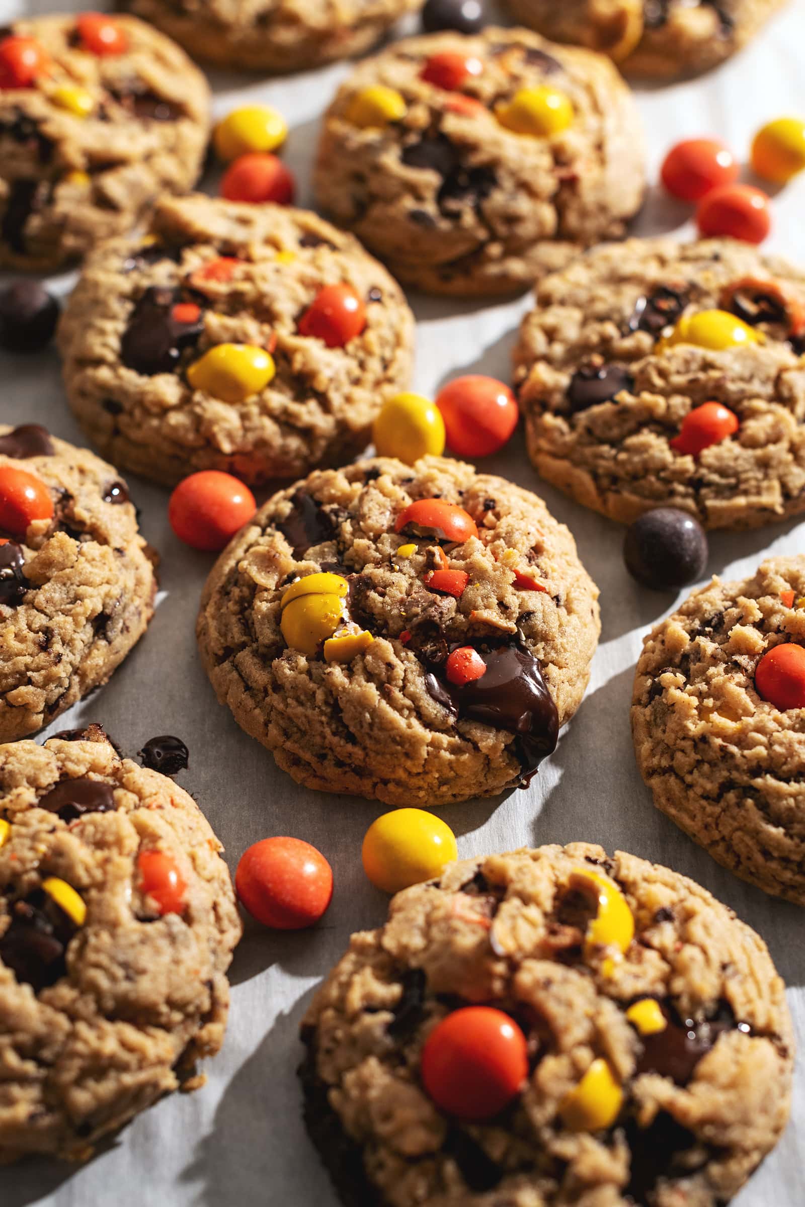 Reese's pieces peanut butter cookies with pools of melted chocolate scattered on parchment paper.