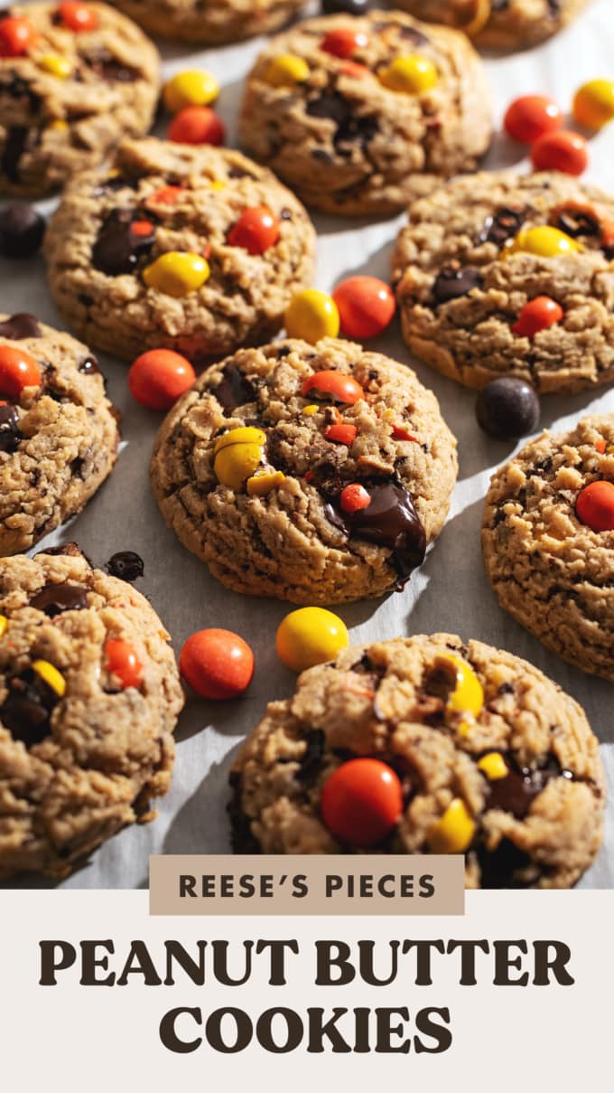 Reese's pieces peanut butter cookies with pools of melted chocolate scattered on parchment paper.