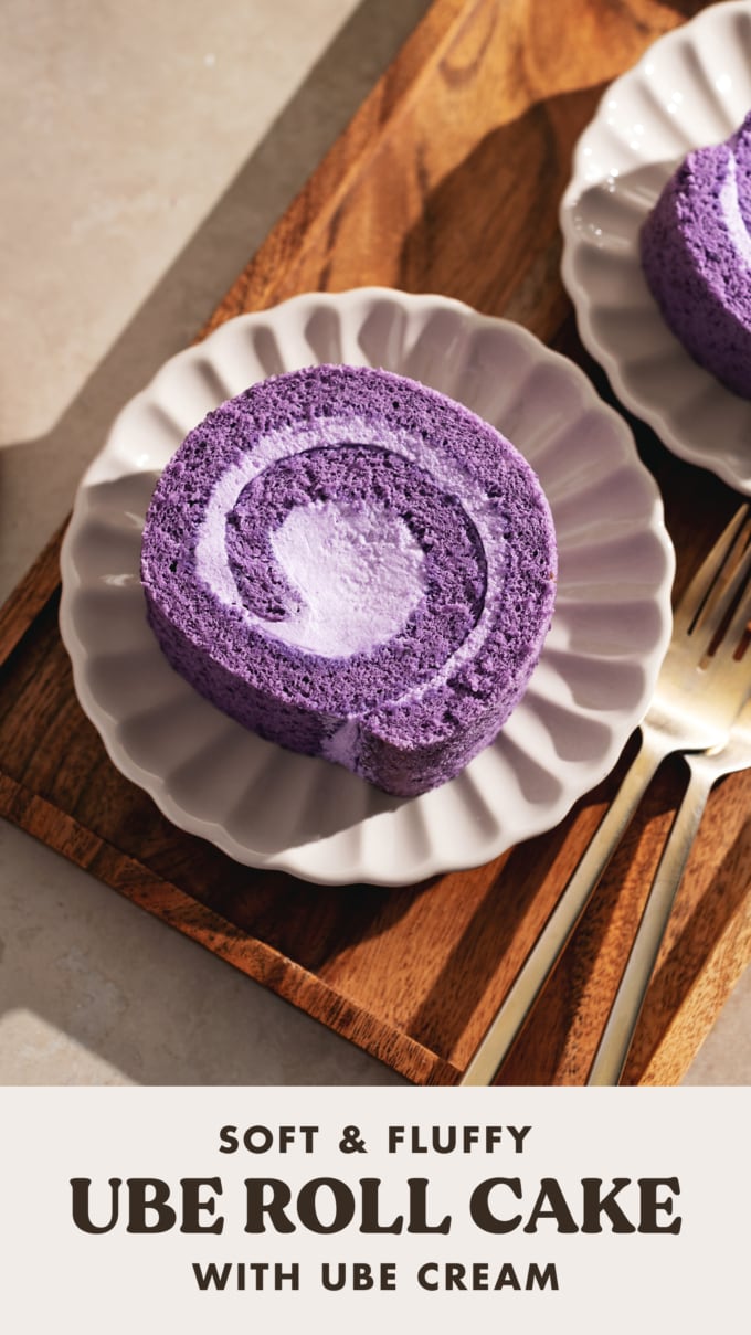 Top down view of a slice of ube roll cake on a scalloped plate on a wooden tray.