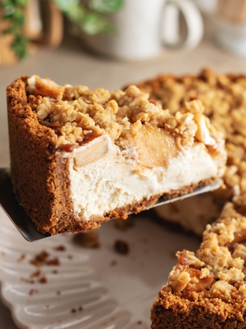 A slice of apple crumble cheesecake lifted up with a cake server.
