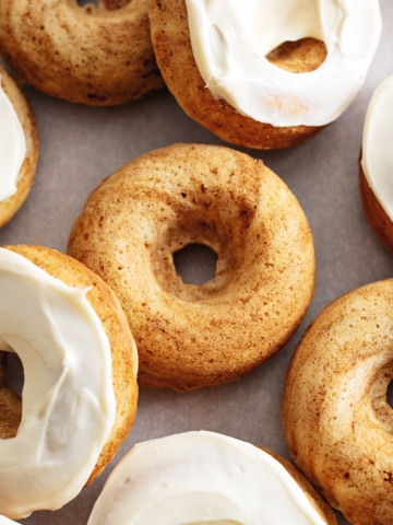 Cinnamon roll donuts scattered on parchment paper, some with cream cheese frosting, some without.