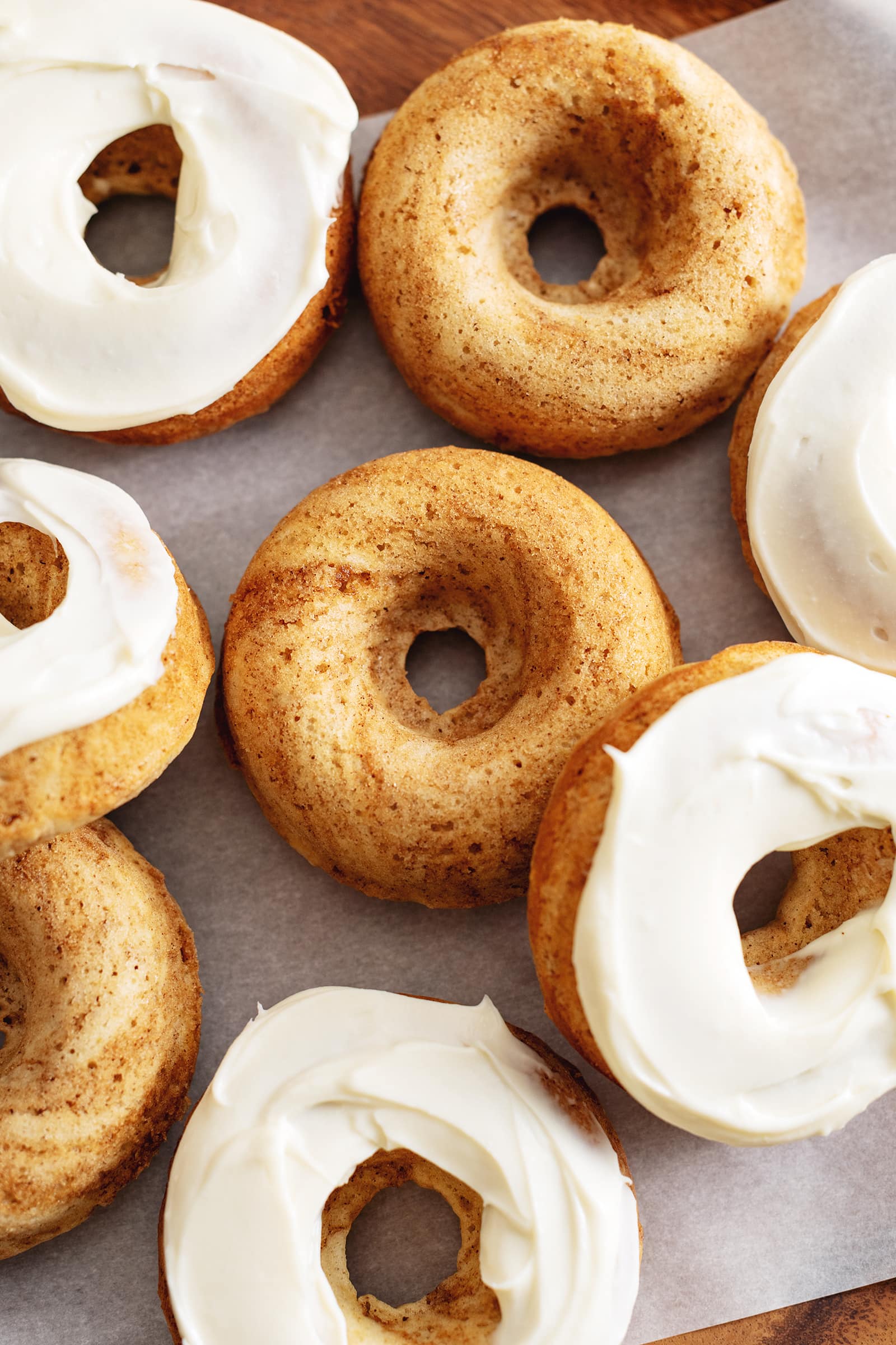 Cinnamon roll donuts scattered on parchment paper, some with cream cheese frosting, some without.