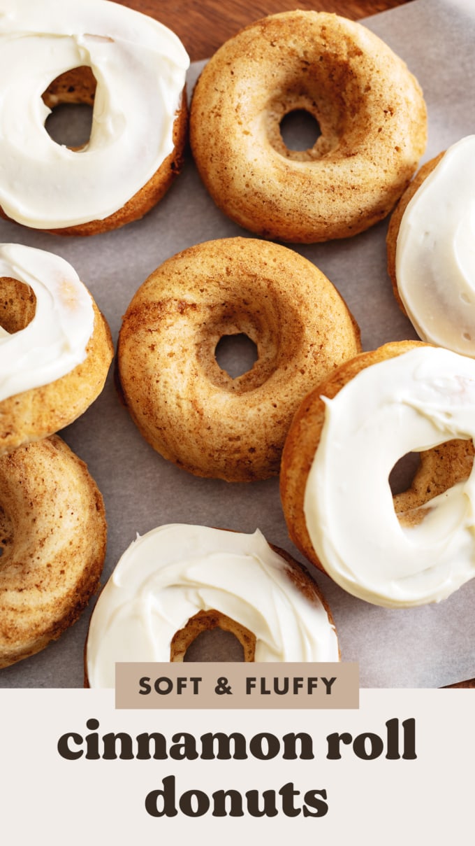 Cinnamon roll donuts scattered on parchment paper, some with cream cheese frosting, some without.
