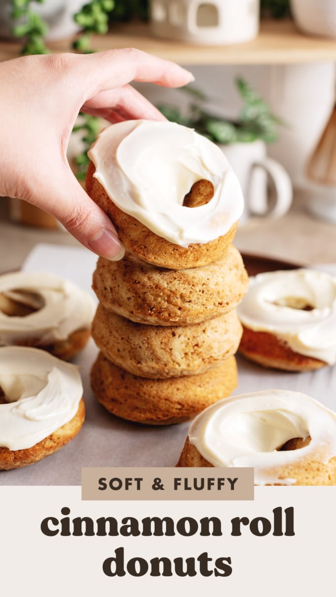 Hand placing a frosted donut on top of a stack of donuts.