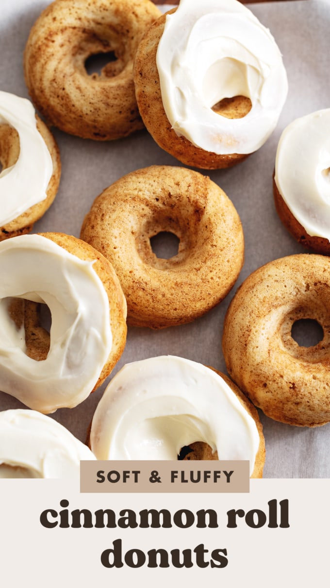 Cinnamon roll donuts scattered on parchment paper, some with cream cheese frosting, some without.