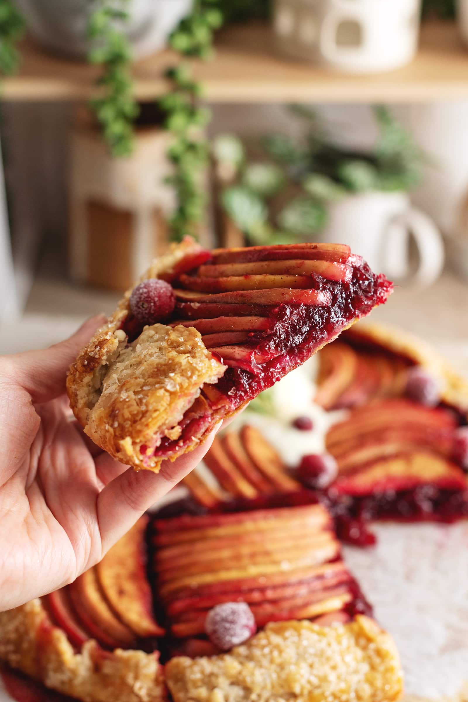 Hand holding a slice of cranberry galette to show the cranberry filling inside.