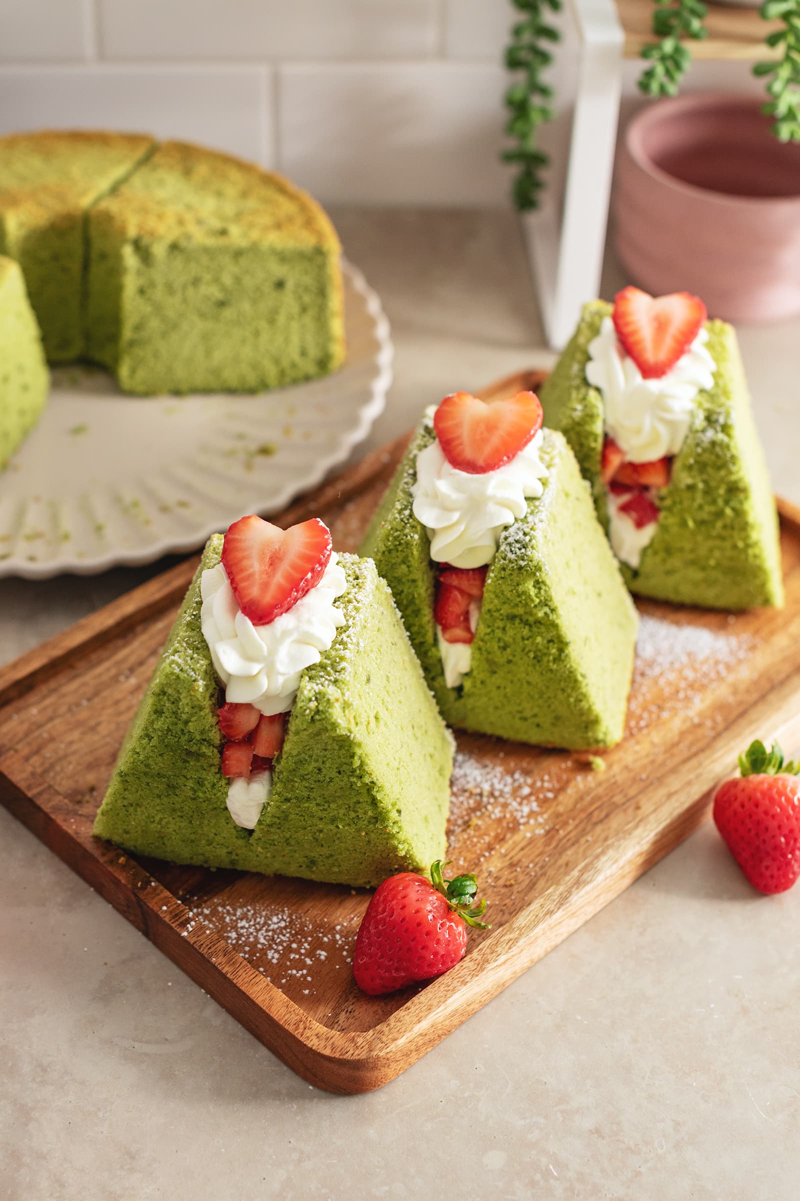 Three matcha chiffon cake sandwiches lined up on a wooden platter.