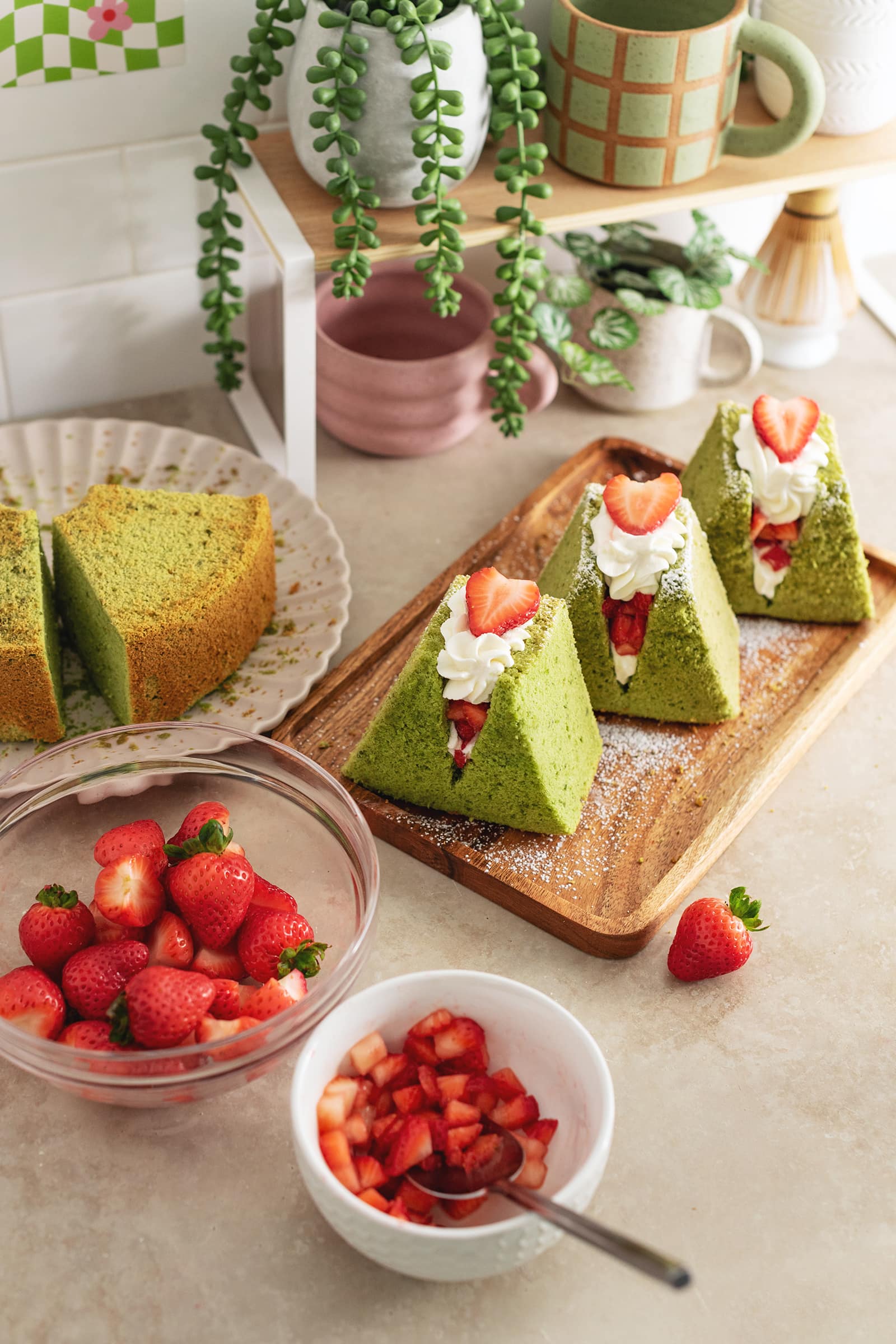 Matcha chiffon cake sandwiches on a wooden platter surrounded by bowls of strawberries.