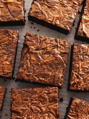 Squares of miso brownies with crackly tops scattered on parchment paper.