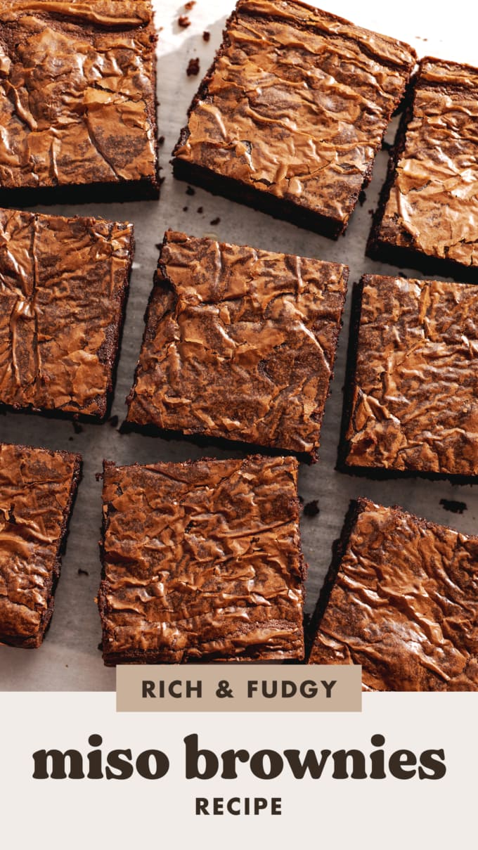 Squares of miso brownies with crackly tops scattered on parchment paper.