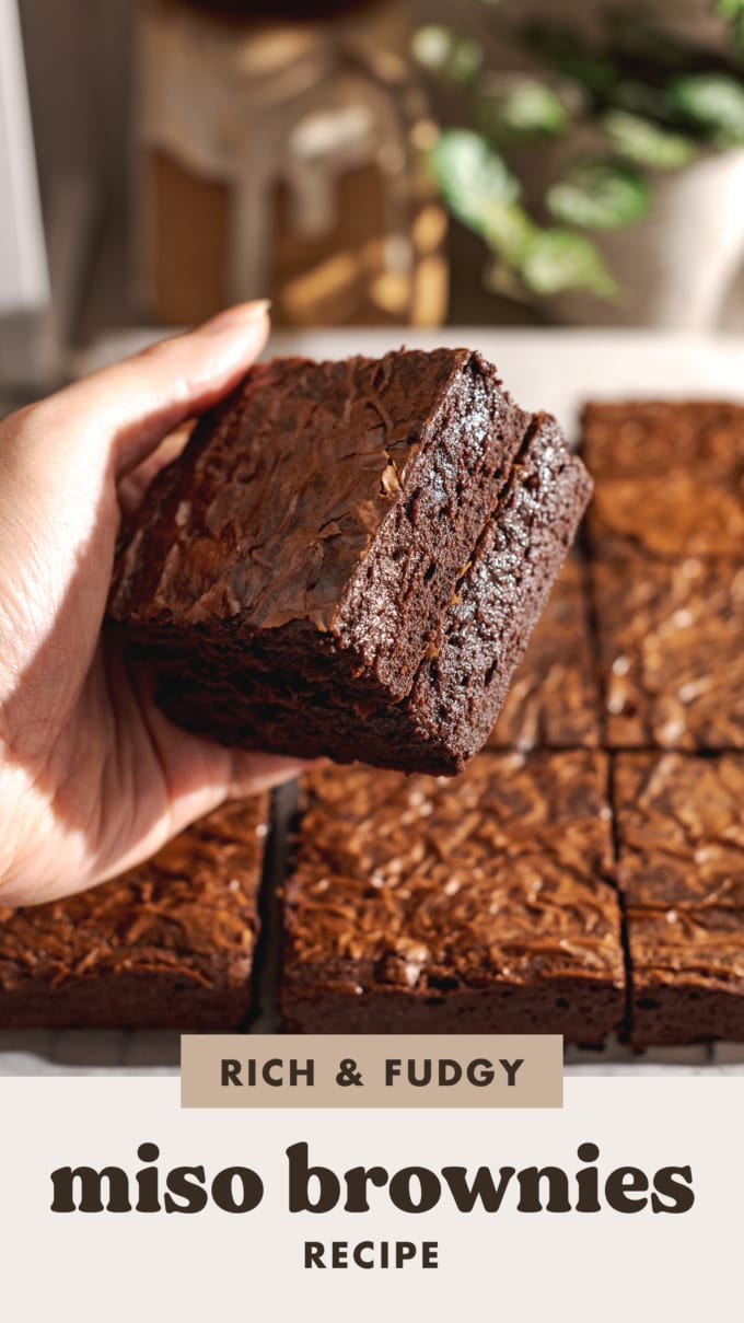 Hand holding a stack of two brownies to show fudgy texture on the side.