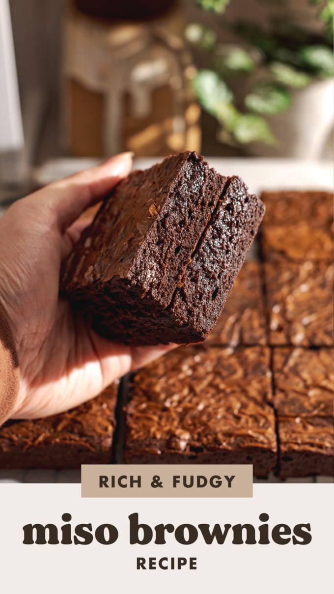 Hand holding a stack of two brownies to show fudgy texture on the side.