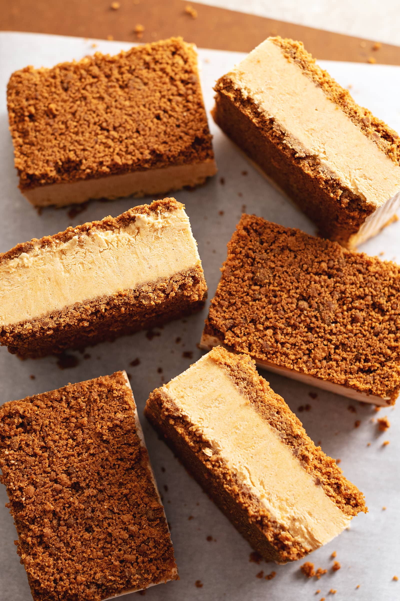 Pumpkin pie ice cream sandwiches scattered on parchment paper with some turned on their sides.
