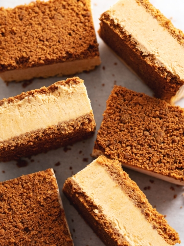 Pumpkin pie ice cream sandwiches scattered on parchment paper with some turned on their sides.