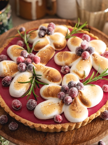 A cranberry meringue tart on a wooden cake stand.